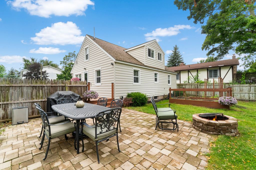Backyard brick patio with a table, chairs and a fire pit, and two white houses.