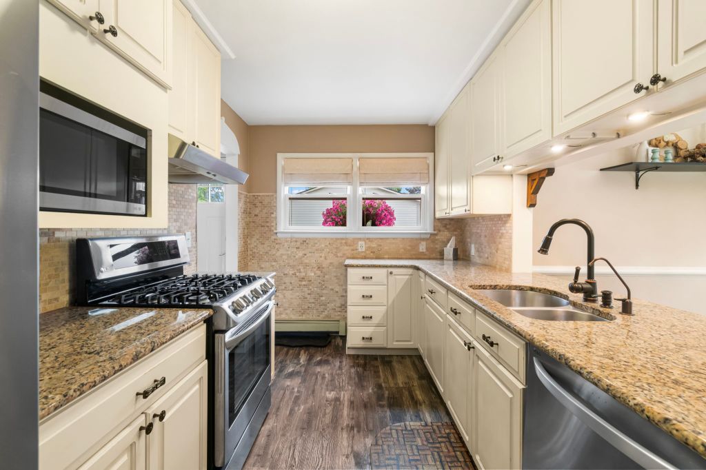 A well-equipped kitchen with brown granite countertops, white cabinets, and stainless-steel appliances. The room is bright...