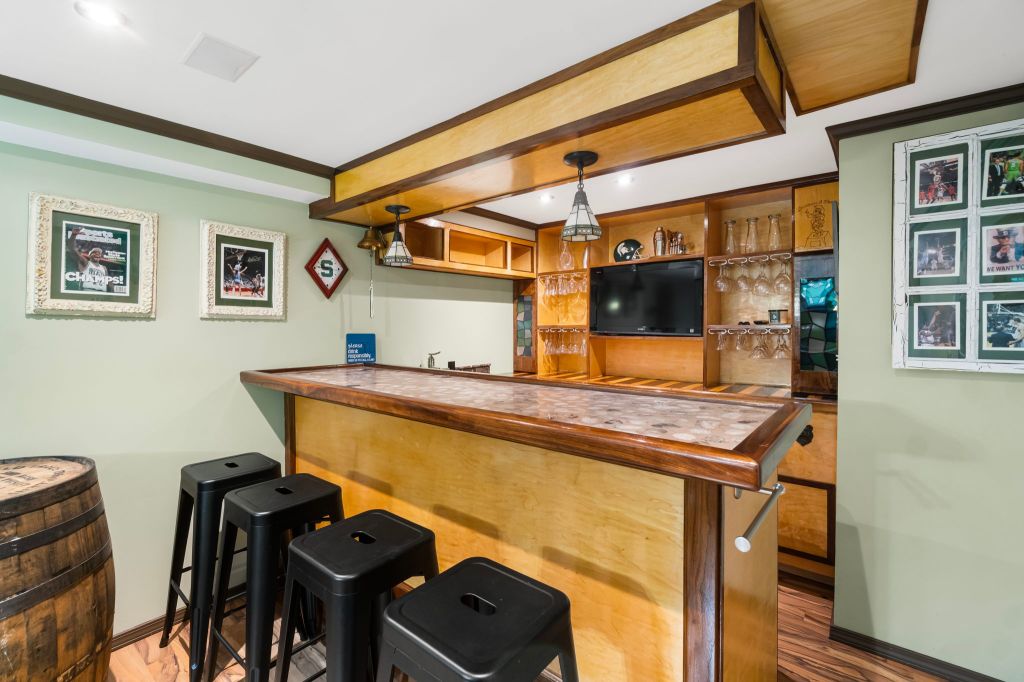 The image shows a home bar with a wooden counter and stools. The wall behind the counter is painted mint green, and the wa...